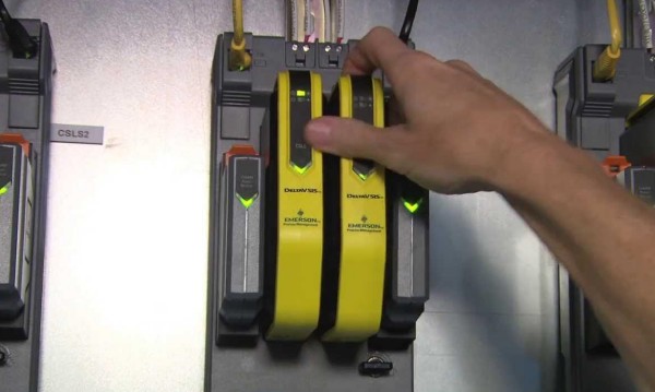 A technician's hand carefully adjusting a yellow Emerson DeltaV SIS module in a DCS control rack during predictive maintenance.