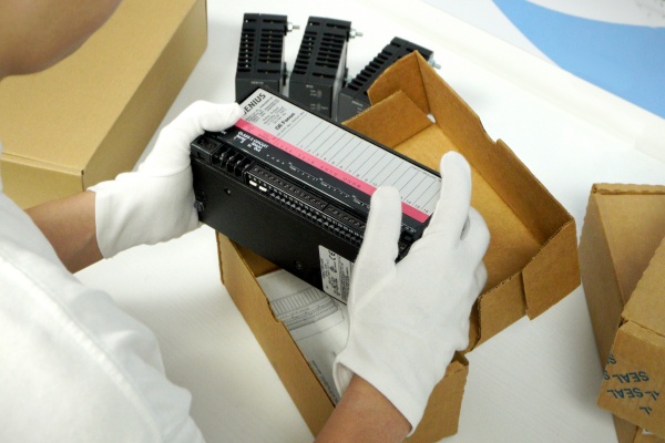 A person wearing white gloves carefully unpacking a component for Modern Gas Turbine Surge Control Systems from a cardboard box.